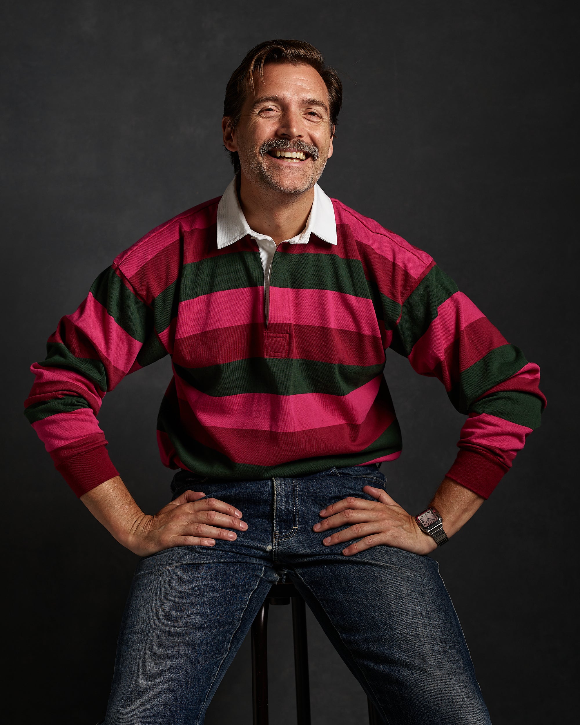 Image of Community Clothing Founder Patrick Grant sat on a stool wearing a pink and green striped rugby shirt.
