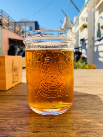 A beer sits on a table outside in a glass with a sketching of a dog's face.