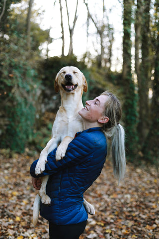 A woman holding her dog in the woods. The dog is smiling with its eyes closed.