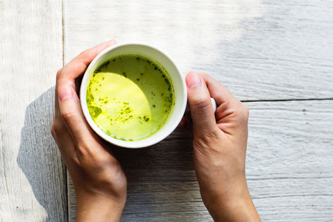 A woman holds a mug of matcha tea after matcha preparation.