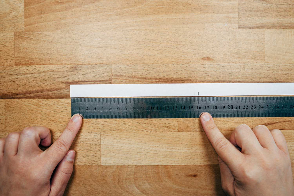 Um deinen Handgelenkumfang zu bestimmen, miss deinen Papierstreifen flach auf dem Tisch liegend von Anfang bis zum markierten Strich aus.