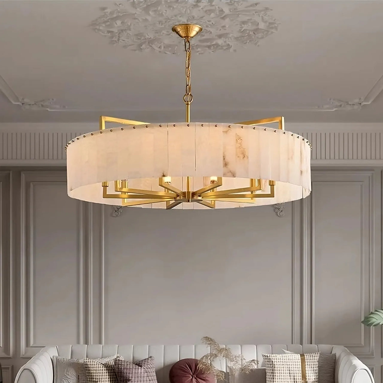 A modern living room features the Morsale West Chester Marble Chandelier, with a gold and cream geometric frame above a white tufted sofa with patterned pillows. Marble accents enhance the space’s contemporary style.