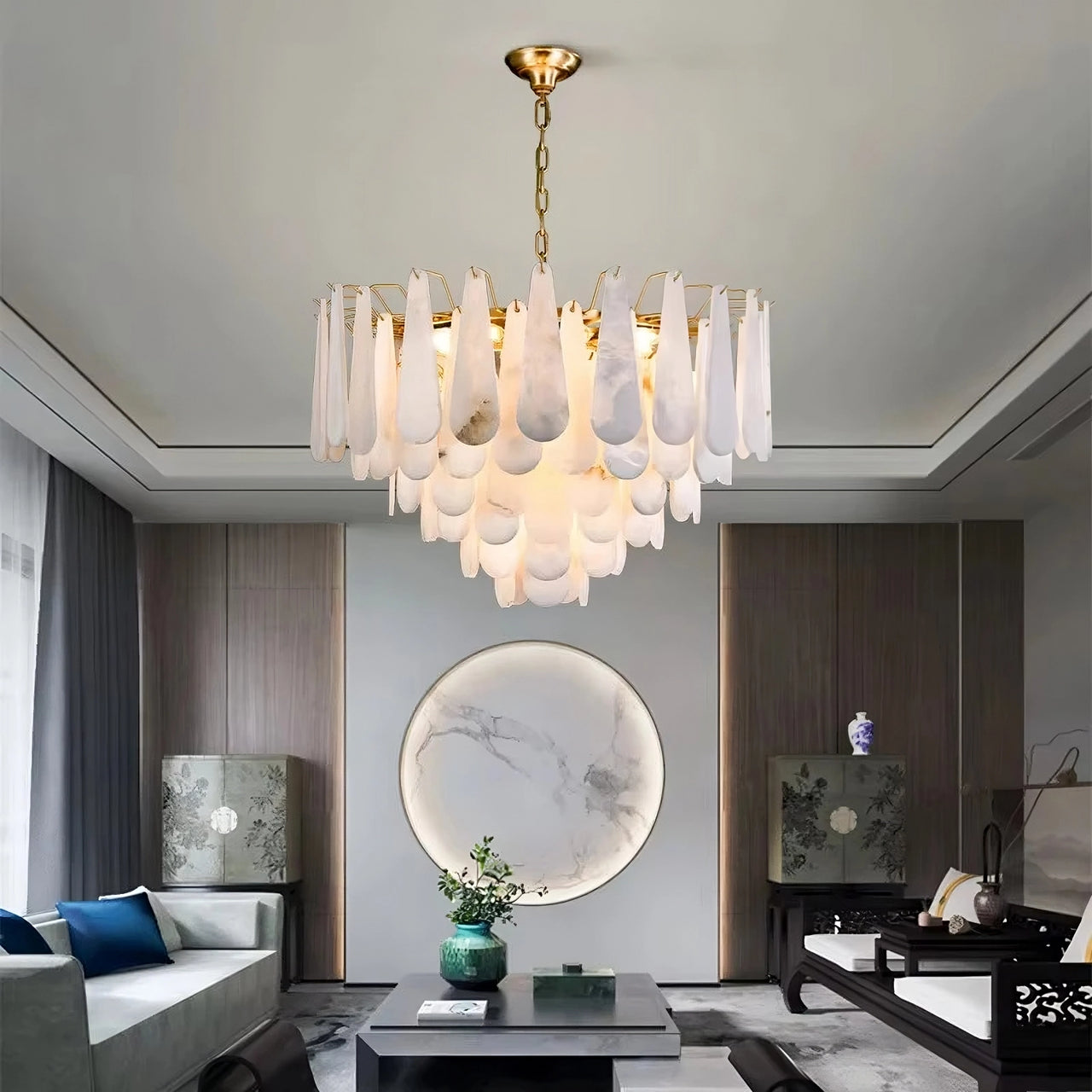 A modern living room features the Morsale Altessa Marble & Copper Chandelier with layered white glass, complemented by contemporary furniture, circular natural marble wall art, and soft natural light through tall windows with sheer curtains.