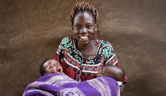 一名婦女向著鏡頭微笑，手裡抱著兩名用紫色毛巾包裹著的嬰兒。