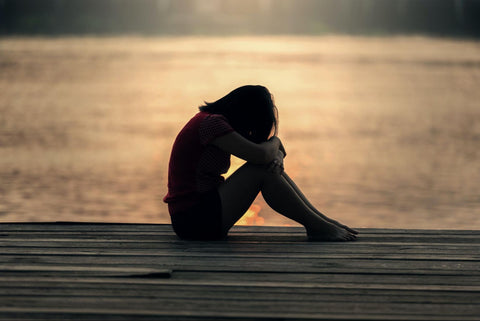 anxious woman sits outside hugging knees