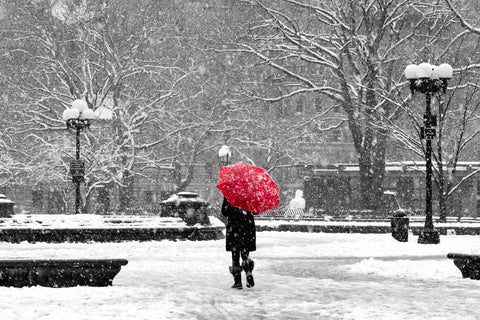 A woman with a red umbrella standing in a snowfall