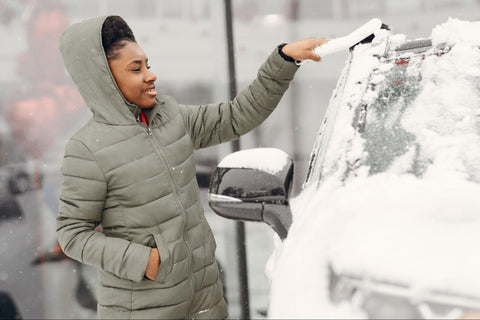 woman cleaning snow from car with snow brush