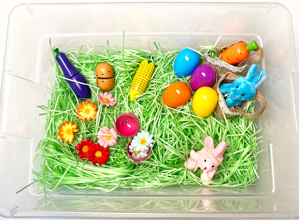 Easter sensory bin for preschoolers with green paper grass, plastic eggs, and other spring themed items