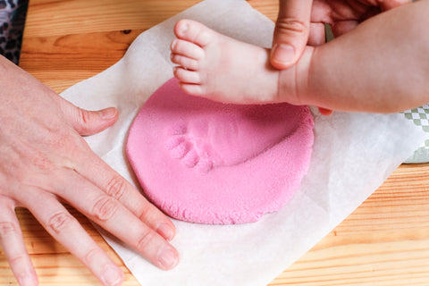 A parent presses a baby's foot into dough for a Valentines Day keepsake.