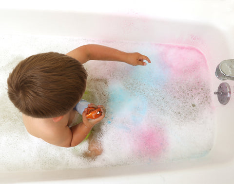 Child in bathtub spraying colors in the bubbles.