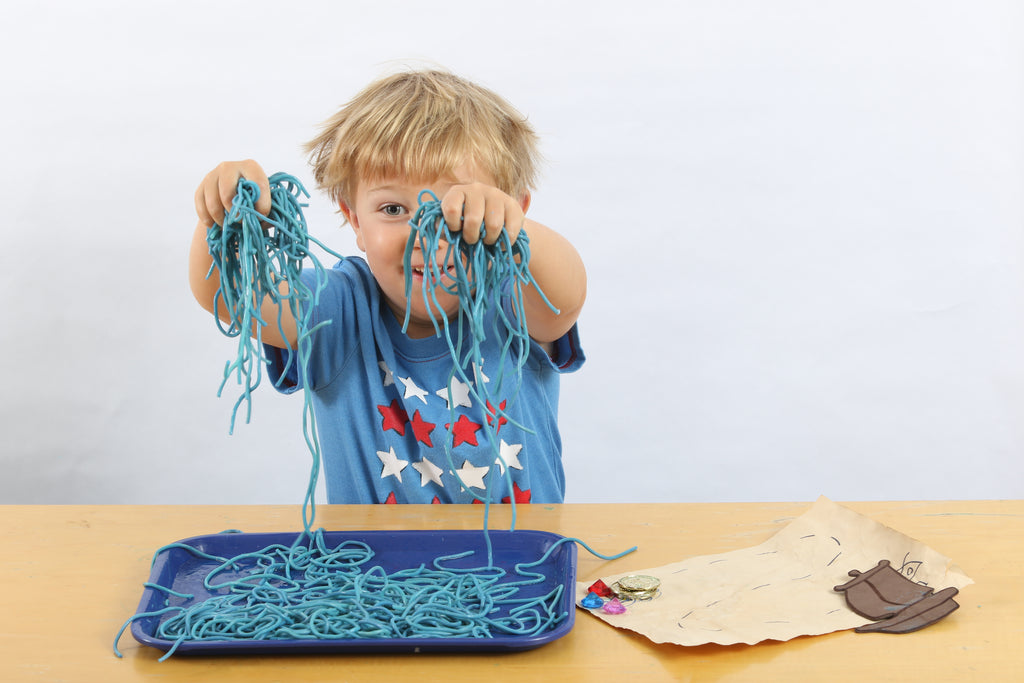 Child plays with spaghetti to practice sensory play.