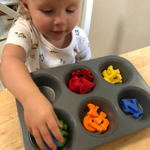 A child organizing items with a cupcake tray.