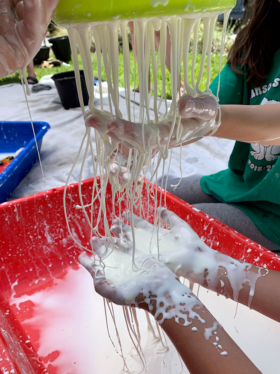 kids' hands under a colander with oobleck liquid flowing out