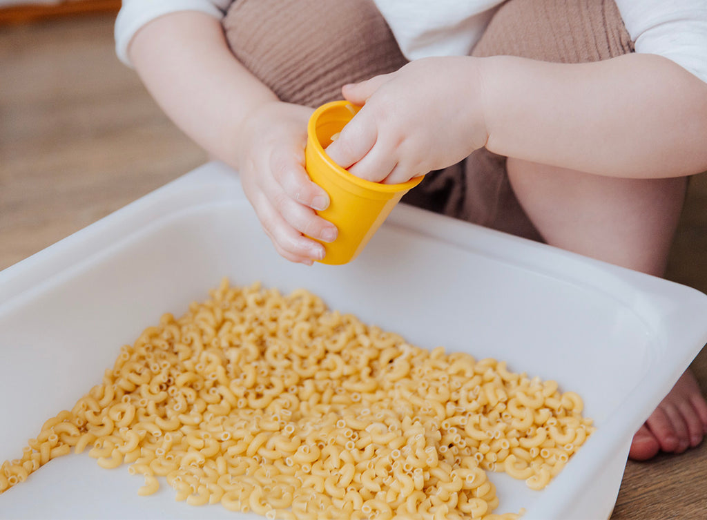 Toddler using dried pasta for a sensory bin base material