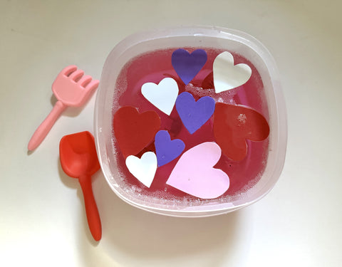 Pink gelatin and foam Valentine's Day hearts in a container with scooper spoons.