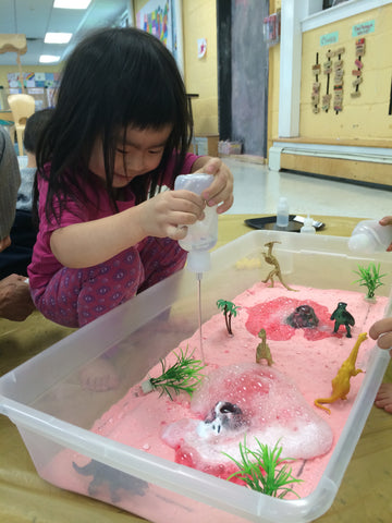 Child pours water into a sensory play bin.