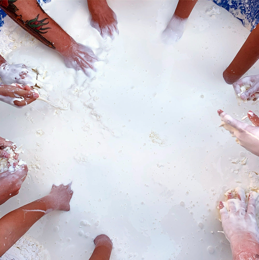 a group of peoples' hands submerged in a baby pool full of oobleck