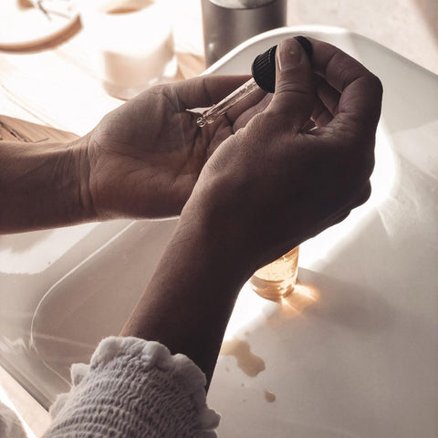 Female dropping essential oils into hands over sink