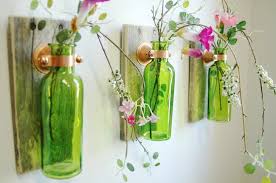 Green bottle attached to a wall with flowers inside
