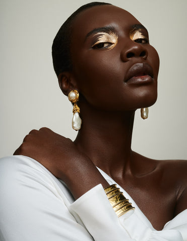 Black model with gold eyeshadow and white top wearing pearl drop earrings