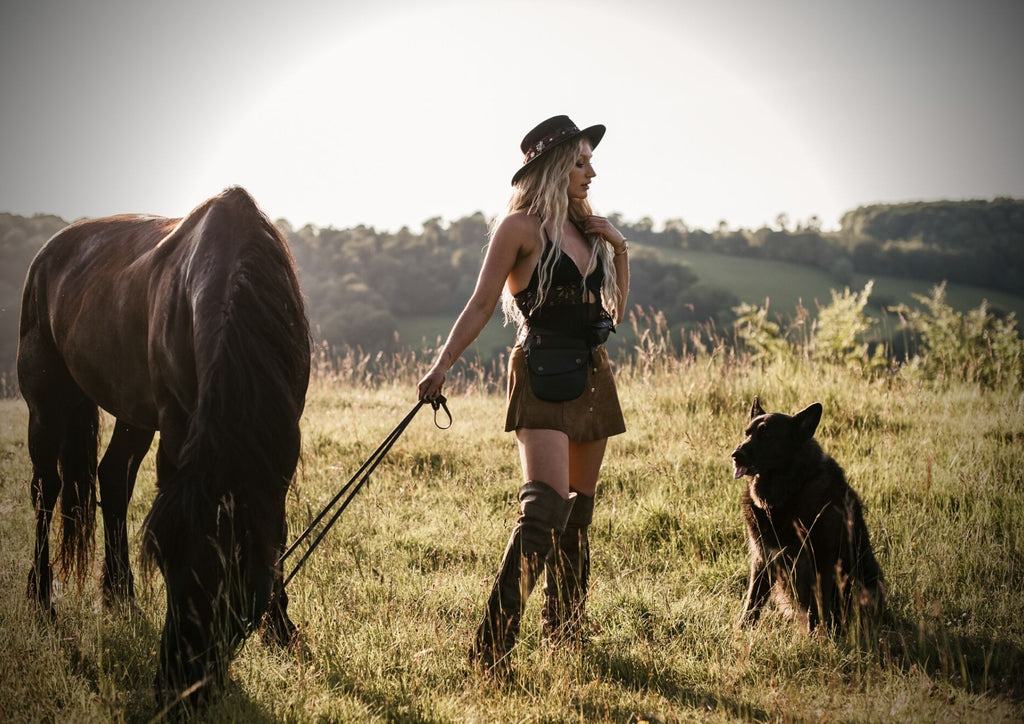 Bathed in the golden glow of a radiant sunset, a woman and her companions, a horse and a dog, find solace on a tranquil hillside. Her leather belt bag combines fashion and functionality, allowing her to keep her essentials close while sharing quiet moments with the man by her side, embracing the serenity of the twilight hour. (Keywords: hillside, sunset, horse, dog, leather belt bag, fashion and functionality, quiet moments, serenity, twilight hour)