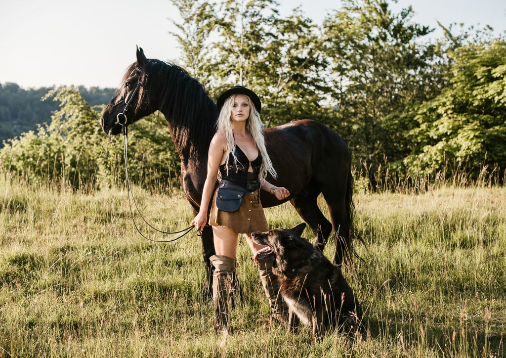 In the heart of the woods, a woman enjoys a peaceful stroll alongside her majestic horse and devoted dog. Her leather belt bag adds a touch of sophistication to her outdoor ensemble, combining practicality and style in perfect harmony. (Keywords: woods, horse, dog, leather belt bag, peaceful stroll, sophistication)