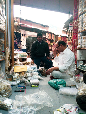 window shopping in pushkar, a man is sitting on the floor of his small shop with piles of gemstines and jewellery around him 