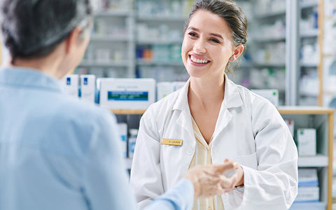 Smiling white-coated pharmacist giving her customer advice about medicine to try for his allergy symptoms