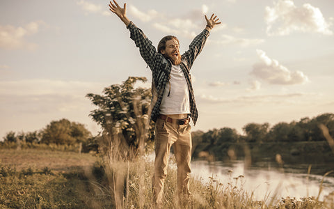 Man jumping for joy on a grassy river bank on a golden summer’s day – no seasonal allergies here or he has them under control