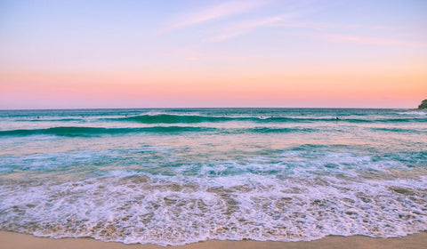 Sunrise on a beach and waves with surfers preparing to surf it