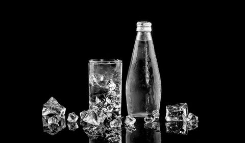 Glass water bottle sitting alongside a glass of water with ice