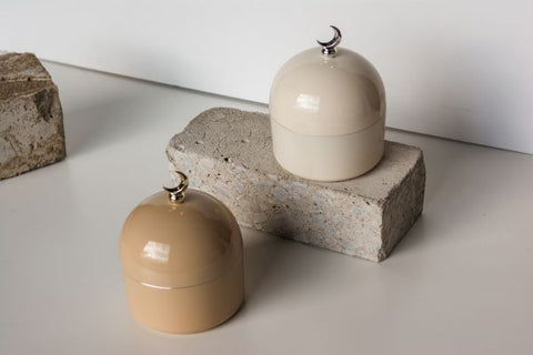 Aesthetic photo of two dome shaped decorative jars, with crescent moon handle. One is set on a concrete brick.