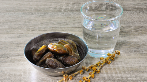Dates in a bowl next to a glass of water.
