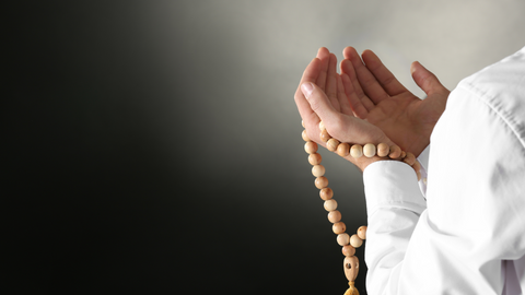 Person raising hands in dua, holding tasbih beads.