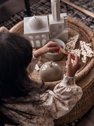Young girl pulling a slip of paper from a Moon Dome Jar and reading what's on the paper.  Next to the Jar, sits the Pearls of North Africa Mosque & Minaret, inside a shallow, round, woven basket atop a coffee table.