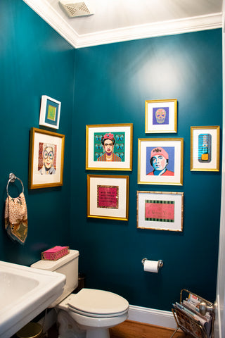 Various framed needlepoint pieces hanging on wall in bathroom