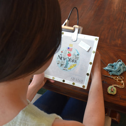 Customer stitching New York needlepoint canvas using portable needlepoint light to clipped onto stretcher bars