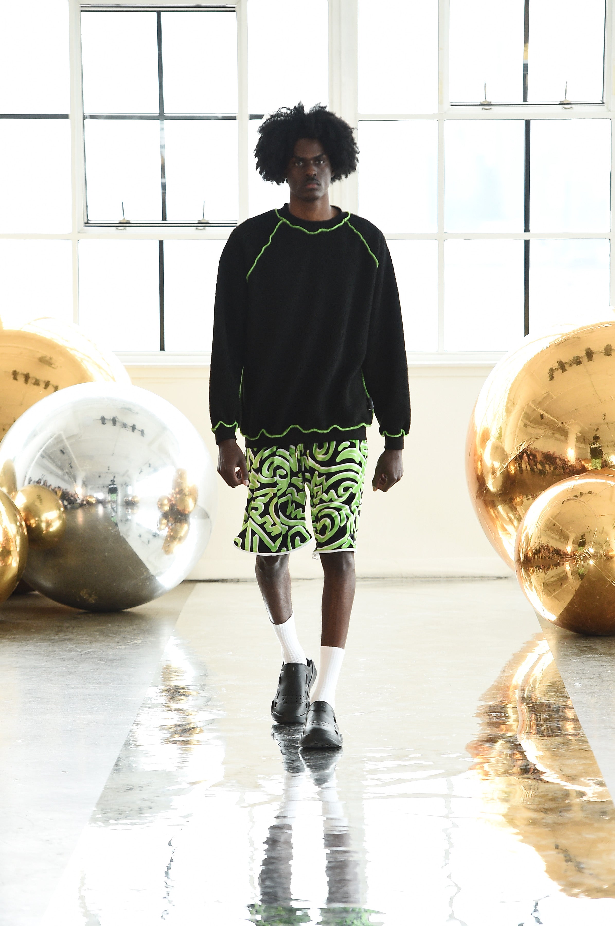 NYC model Daniel walks the Catwalk for NYFW FW/24  at Canoe Studios in Manhattan wearing Bellisa X unisex streetwear featured in Fashion Week Online. Outfit: Black sherpa sweatshirt with white monogram graphics with Green Abstract Velvet Shorts, Socks and Champion Sandals