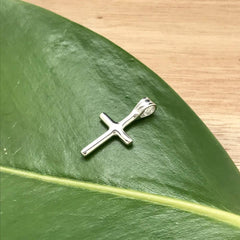 Silver cross pendant on green leaf
