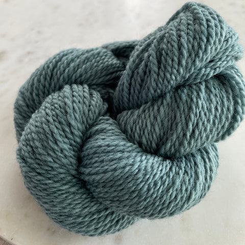 a little bundle of soft teal yarn sits twisted on a marble plate