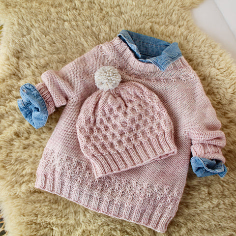 soft pink baby sweater and hat sitting on top of a sheepskin. 