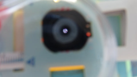 A hand lens in front of a Foldscope showing a magnified view of the microscope slide inside the microscope