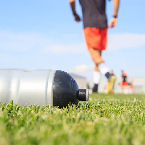 Close up of a water bottle on a grass field with people playing soccer in the background.
