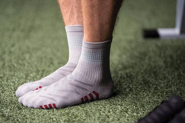 Close up on man's feet wearing Base33 Sport Crew Socks in Grey standing on turf green fake grass.