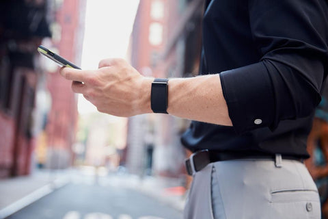 Hombre de pie en la calle que muestra el brazo derecho sosteniendo el teléfono celular y la manga sin moverse con el uso de FLXCUF negro