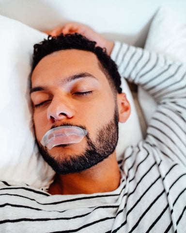 A man lays in bed sleeping with SomniFix mouth tape on to prevent snoring and improve sleep quality.