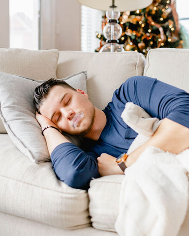 A man takes a nap on his couch while wearing SomniFix mouth tape for better sleep quality and snoring prevention.