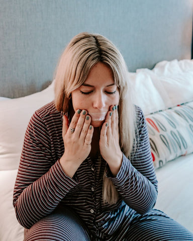 A woman sits in bed and applies mouth strips before sleeping to prevent snoring and promote nasal breathing. 