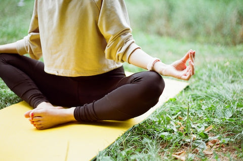 A woman in black leggings and a brown sweater sits on a yoga mat.