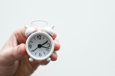 Person holding white mini bell alarm clock.